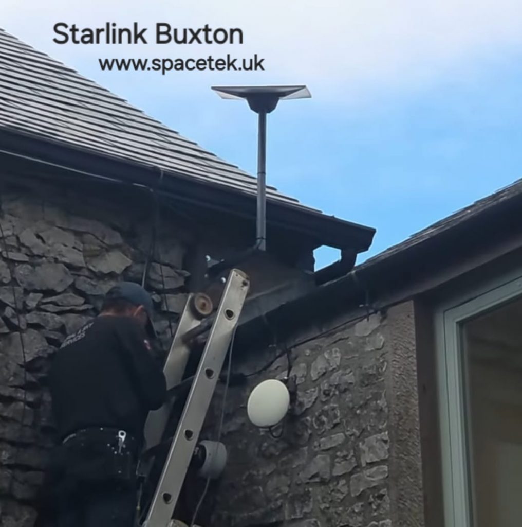 Maintenance worker on a ladder installing a Starlink satellite dish on a stone house exterior.