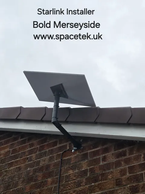 Starlink dish on a dark angled wall mount below the roof edge of a brick bungalow in Bold Merseyside