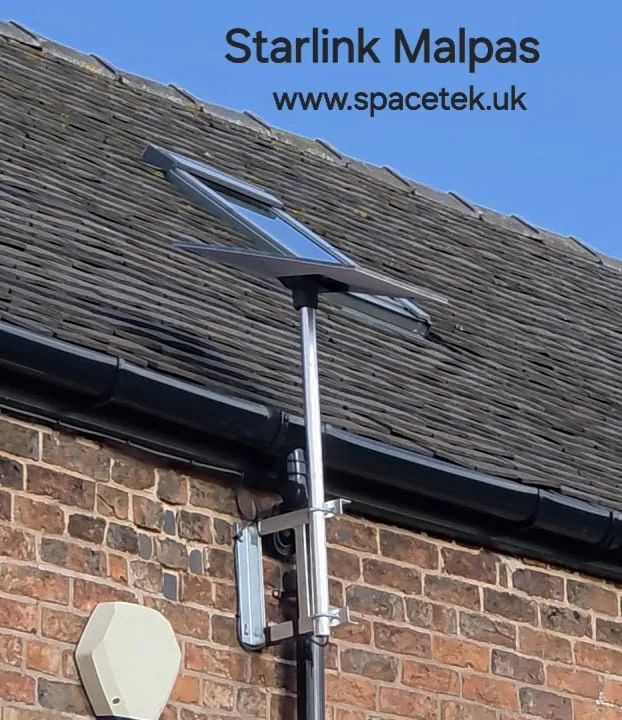 Starlink dish on a metal pole and twin wall brackets beside a slate roof in Malpas